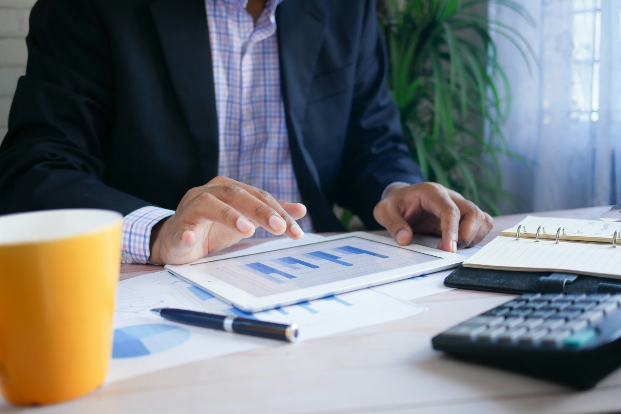 Business professional reviewing financial charts on a tablet beside a calculator and notebook
