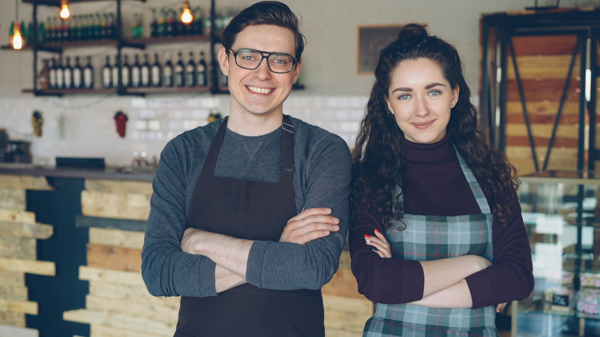 Two people wearing aprons standing inside a café